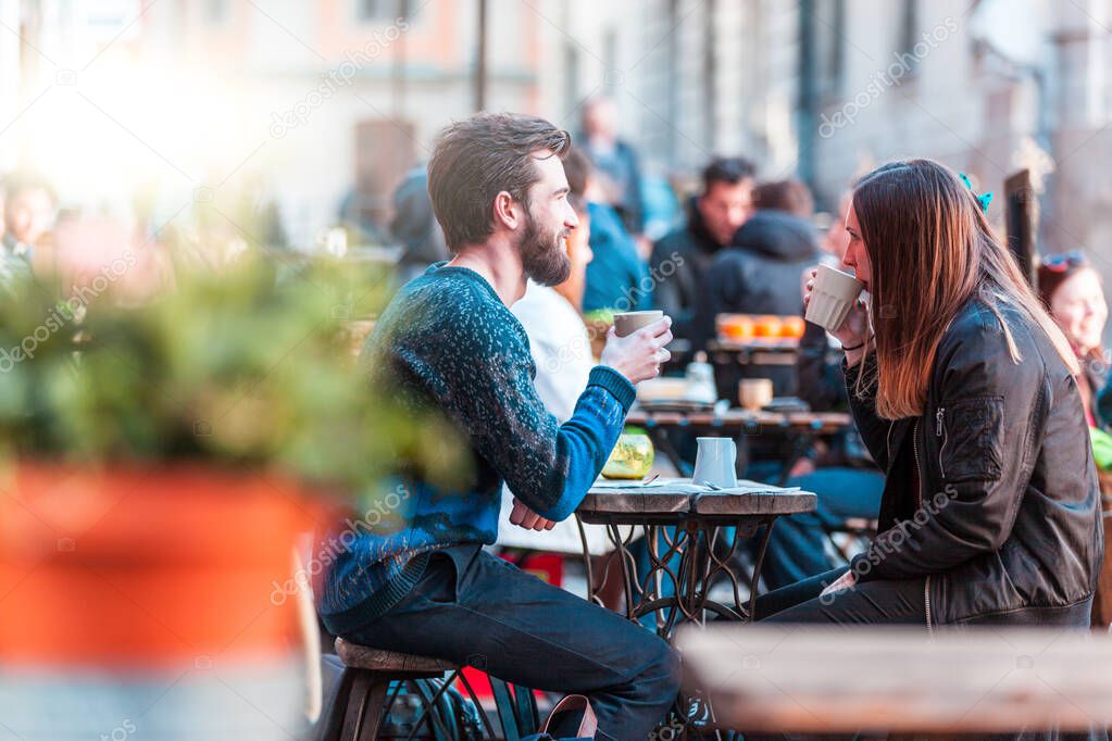 Hipster friends drinking coffee in Stockholm old town - Young couple sitting face to face outdoors and enjoying time together - Open bar with social distancing in place