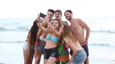 Sahilde selfie çeken çok kültürlü bir arkadaş grubu, sosyal medyada paylaşmak için cep telefonuyla fotoğraf çeken gençler, yaşam tarzı ve arkadaşlık kavramları.