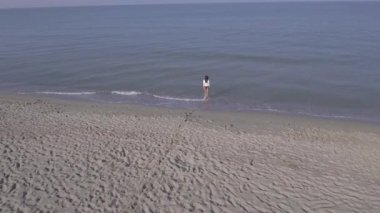 Deniz kıyısında yürüyen genç bir kadın kumsalda yalnız başına kumdan denize doğru yürüyen ve rahatlatıcı yaşam tarzı ve yaz kavramları.