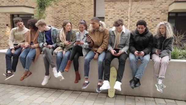 Мультиетнічна група людей з смартфонами в місті - велика група людей, які сидять разом і дивляться на свої телефони - соціальна медіа концепція і залежність, тисячолітній спосіб життя в Лондоні. — стокове відео