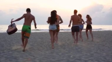 Sahilde denize doğru koşan bir grup insan, deniz kenarında birlikte vakit geçirip gün batımında eğleniyorlar, yaşam tarzı ve arkadaşlık kavramları.