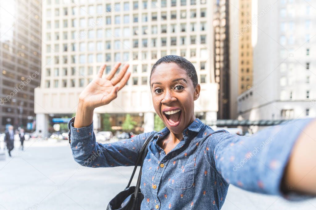 Happy woman waving to the camera and laughing - Black woman with short hair taking a selfie or videocall in Chicago - Lifestyle and technology concepts