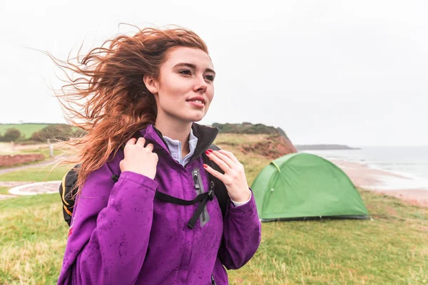 ハイキングやキャンプ旅行の美しい女性の肖像画 海辺の崖のテントの前にポーズバックパックやハイキングギアを身に着けている若い女性 旅行や冒険の概念 — ストック写真