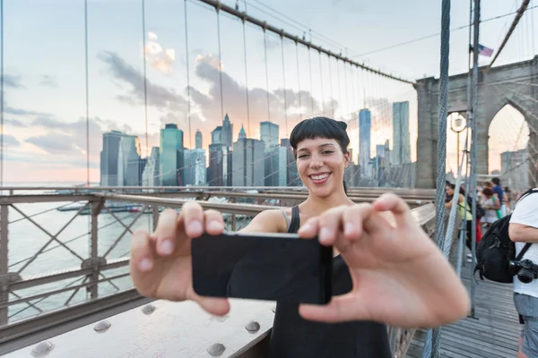 Ganska ung kvinna tar selfie på brooklyn bridge — Stockfoto