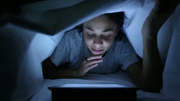 ベッドのシーツの下でデジタル タブレットを使用してひそかな女性 — ストック動画