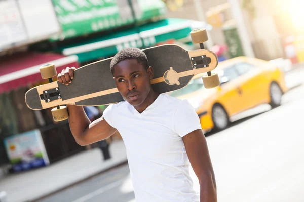 Schwarzer Junge läuft mit Longboard durch die Stadt — Stockfoto