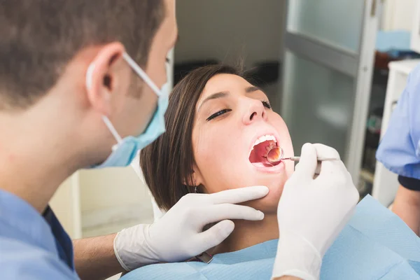 Dentista esaminando denti paziente con uno specchio bocca — Foto Stock