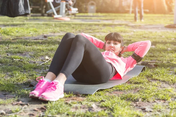 Junge Frau macht Bauchmuskelübungen im Park. — Stockfoto