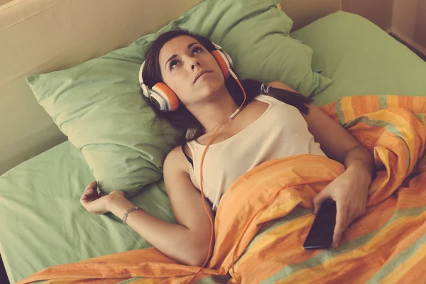 若い女性の聞く音楽をヘッドフォンでベッドの上 — ストック写真
