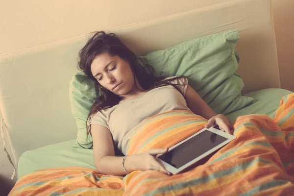 Mulher jovem que cai adormecido ao usar o comprimido digital na cama — Fotografia de Stock