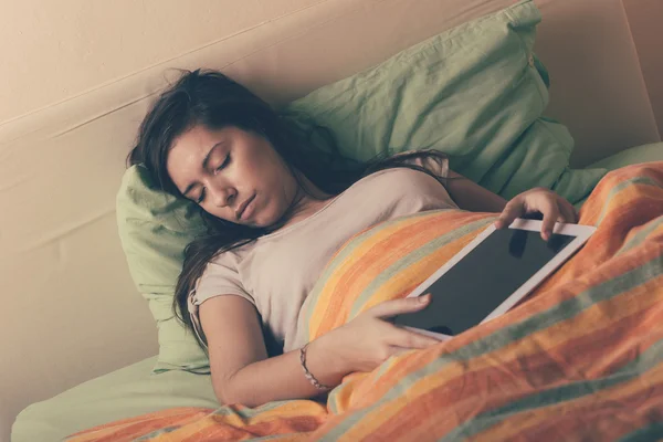 Mulher jovem que cai adormecido ao usar o comprimido digital na cama — Fotografia de Stock