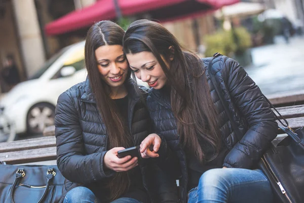 Två kvinnliga tvillingar tittar på en smart telefon — Stockfoto