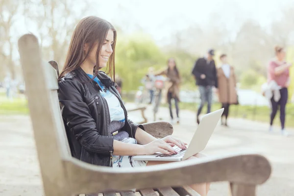 Jonge vrouw met behulp van computer op park in Londen — Stockfoto