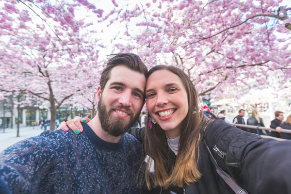 Hipster couple taking a selfie in Stockholm with cherry blossoms — Stock Photo, Image