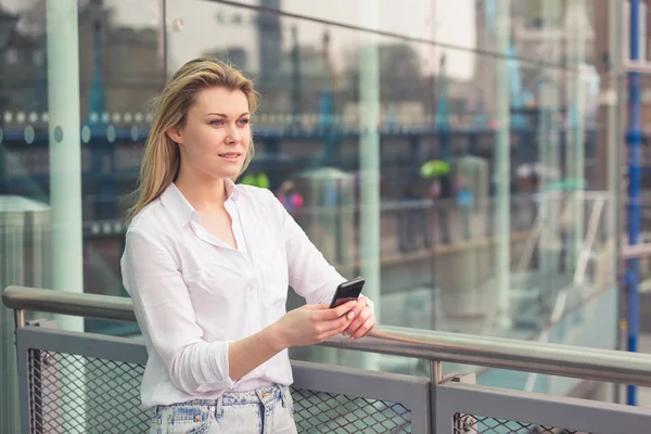 Młoda kobieta wpisując na inteligentny telefon z tłem przeszklone — Zdjęcie stockowe