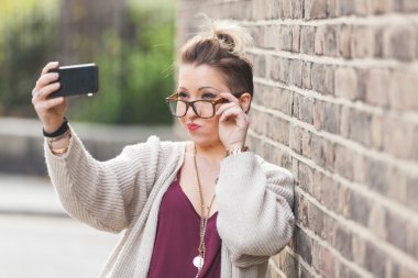 Tuğla karşı bir selfie alarak hipster kadın duvar Londra'da.