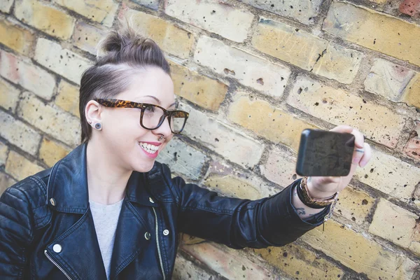 Femme hipster prenant un selfie contre un mur de briques à Londres . — Photo