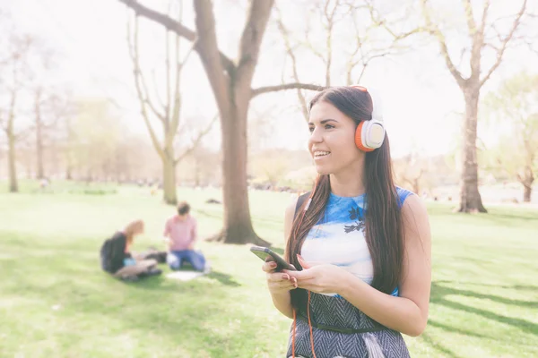 Jonge vrouw luisteren muziek in het park in Londen — Stockfoto