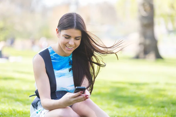 Молода жінка, дивлячись на смарт-телефону в park в Лондоні — стокове фото