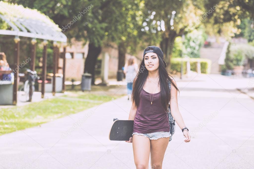 Beautiful girl walking at park holding a skateboard.