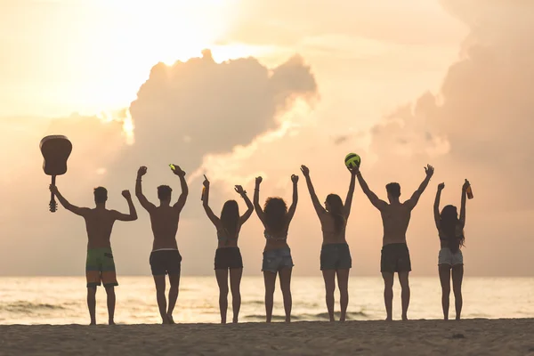 Grupa przyjaciół, podnosząc ręce na plaży o zachodzie słońca — Zdjęcie stockowe