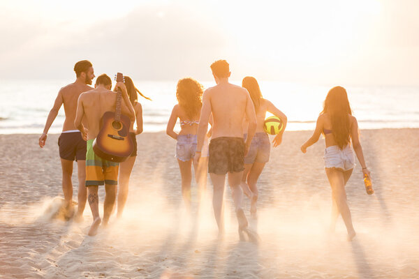 Group of friends walking on the beach at sunset.