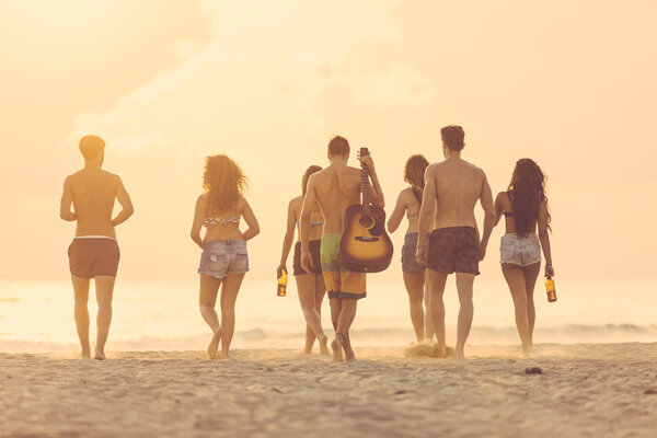 Group of friends walking on the beach at sunset.