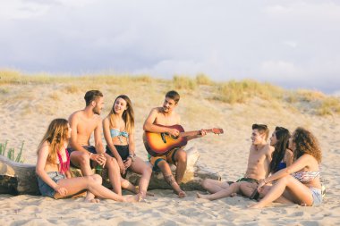 Group of friends singing on the beach at sunset.