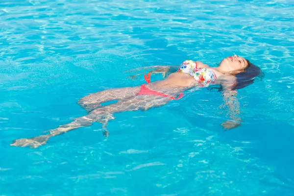 Bella donna sdraiata sulla superficie dell'acqua della piscina — Foto Stock