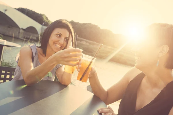 Duas mulheres bonitas tendo um coquetel ao ar livre ao pôr do sol — Fotografia de Stock