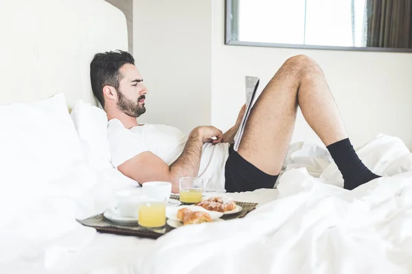 Homme lisant un journal allongé sur le lit — Photo