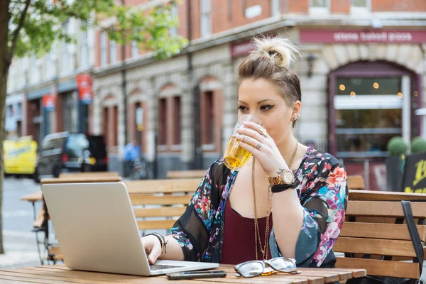 Girl working on her computer and drinking beer — Stock Photo, Image