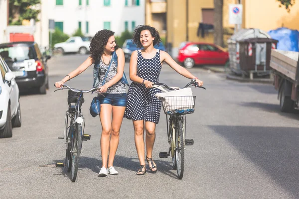 Female friends holding bikes and walking in the city — Stock Photo, Image