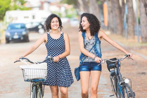 Female friends holding bikes and walking in the city — Stock Photo, Image