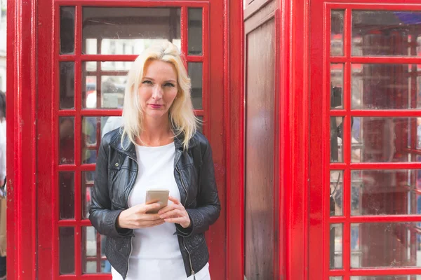 Vacker kvinna stående i London med röd telefonkiosk — Stockfoto