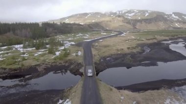 Aerial view of a car driving on a countryside road in Iceland with snow and ice on the side and clouds on background