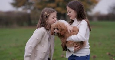 Authentic portrait shot of two little girls smiling and playing together with a dog, with green field and nature on background in a countryside farm in the UK