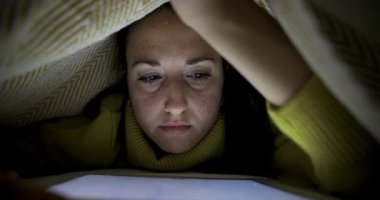 Evdeki kadın battaniyenin altında yatıp dijital tablet - yaşam tarzı ve teknoloji kavramları üzerine okuyor.