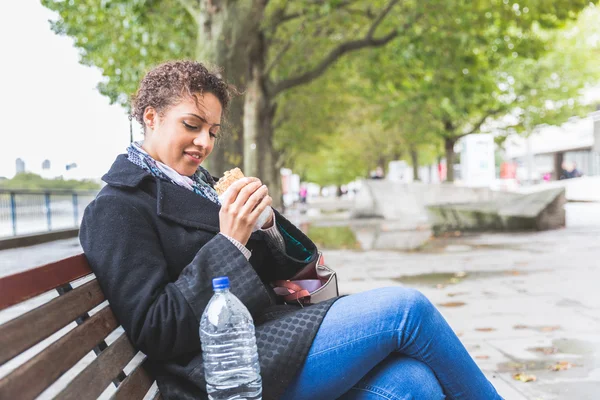 Молодая женщина сидит на скамейке и обедает в Лондоне — стоковое фото