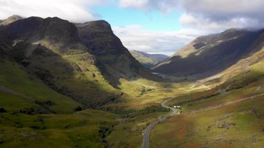 Glencoe yakınlarındaki İskoçya 'nın dağlık bölgelerinden geçen bir yolun insansız hava aracı görüntüsü solda güzel bir günde Glencoe Dağları' nın Üç Kız Kardeşi ile doğa ve seyahat kavramları.