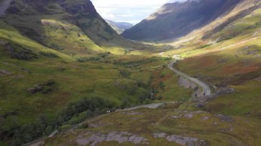 Glencoe yakınlarındaki İskoçya 'nın dağlık bölgelerinden geçen bir yolun insansız hava aracı görüntüsü solda güzel bir günde Glencoe Dağları' nın Üç Kız Kardeşi ile doğa ve seyahat kavramları.