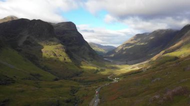 Glencoe yakınlarındaki İskoçya 'nın dağlık bölgelerinden geçen bir yolun insansız hava aracı görüntüsü solda güzel bir günde Glencoe Dağları' nın Üç Kız Kardeşi ile doğa ve seyahat kavramları.