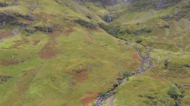 İskoçya 'nın dağlık kesimlerindeki bir şelalenin yeşil bitki örtüsüyle kaplı bir dağın yamacına inişi doğa ve seyahat kavramları güzel manzaralar keşfediyor.