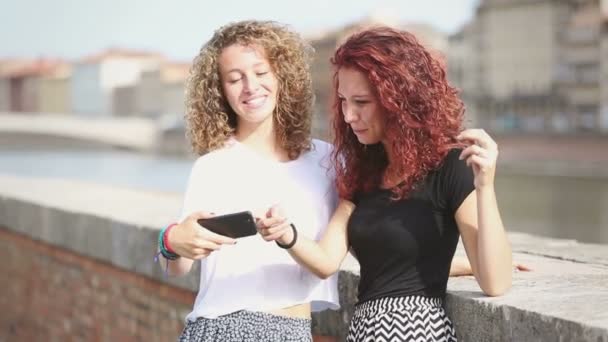 Twee gelukkige meisjes op zoek naar slimme telefoon met stad op achtergrond — Stockvideo