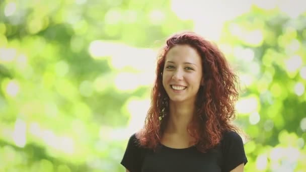 Видеопортрет улыбающейся рыжей девушки в парке — стоковое видео
