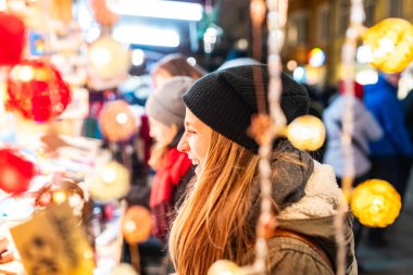 Bere takan genç bir kadın bulanık ışıklarla neşeli bir gece marketine bakarken gülüp gülümsüyor