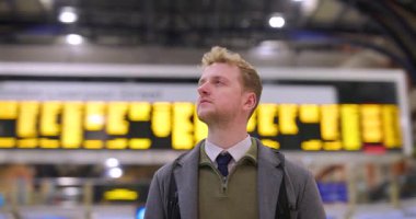 İş adamı bir tren istasyonundaki kalkış tahtasına bakıyor. Genç erkek banliyö çalışanı bağlantısını beklerken zaman çizelgesini kontrol ediyor.