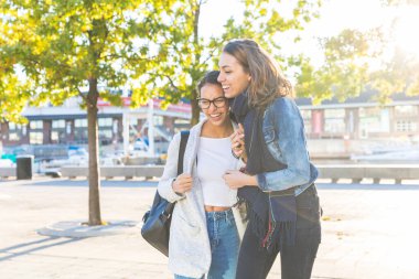 Neşeli bir anı paylaşan iki genç kadın güneşli bir şehirde dostluk ve mutluluğu kucaklıyor.
