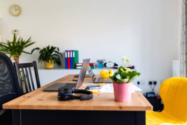 Uzaktan çalışma ve üretkenliği vurgulayan dizüstü bilgisayarlar, kulaklıklar ve çeşitli yeşil santrallerin yer aldığı modern ev ofis çalışma alanı