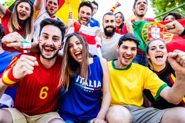 Heyecanlı çok ırklı genç futbol taraftarları ulusal bayrak tişörtleri giyip spor müsabakalarını alkışlıyor ve kutluyorlar.